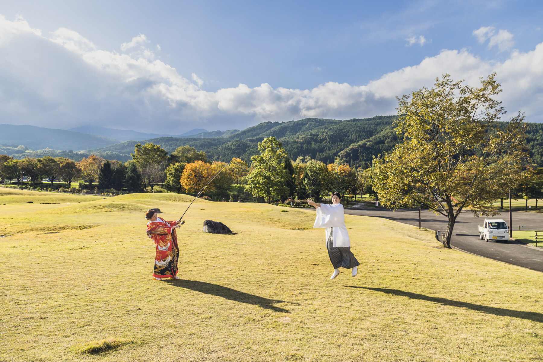 あづま総合運動公園の広い芝生で羽根つきを楽しむ和装の二人と秋の山並み