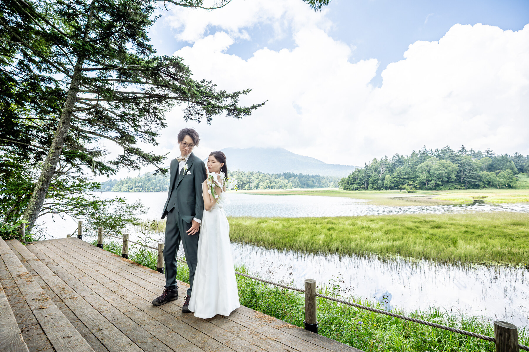 尾瀬の湖畔で山と水辺を背景に手をつなぐ洋装のお二人